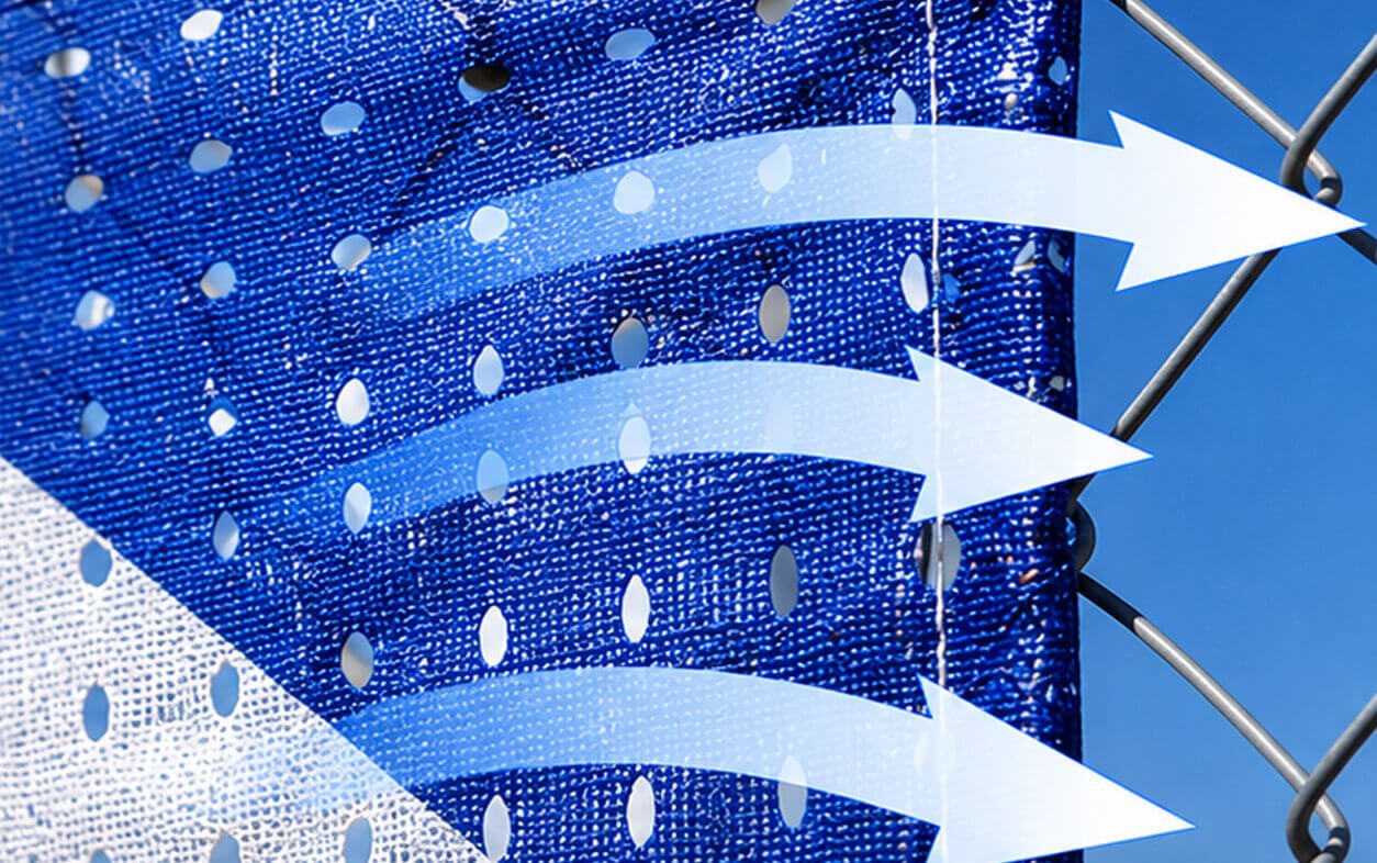 "A close-up of the royal blue mesh fabric banner attached to a chain-link fence under a clear sky. A gold brass grommet is visible, and the clean edges of a printed graphic pattern with sharp blue and white details are sharp and clear, proving the material's printability and permeability to wind.
