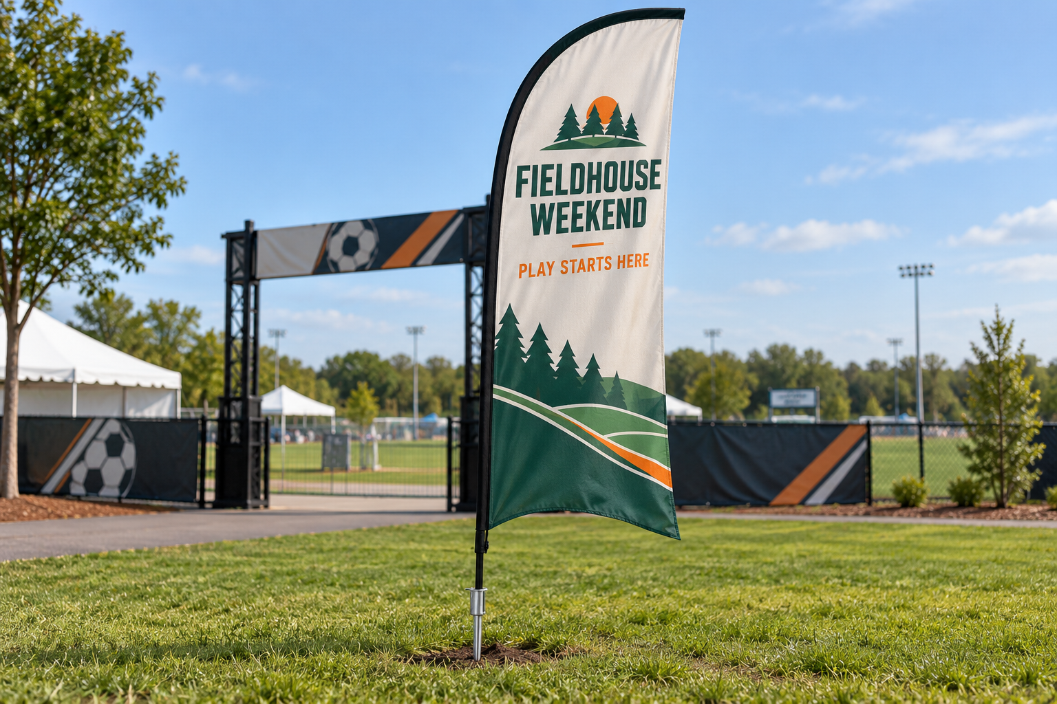 FIELDHOUSE WEEKEND custom feather flag with a pointed ground spike visibly inserted into grass at a sports event entrance
